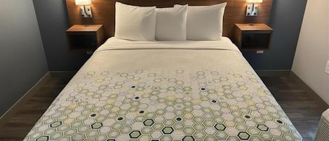 A hotel room with a large bed, two bedside tables with lamps, a headboard, and a painting on the wall.