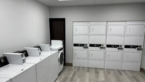 A laundry facility with multiple washing machines and dryers, a wooden floor, and a plain white wall. - Hometownestudios Bradenton (Bradenton)