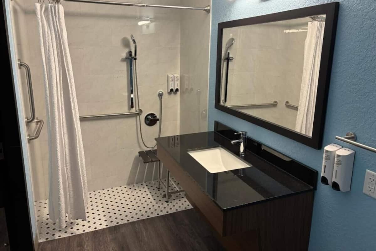 Un baño moderno con ducha, lavamanos, espejo y toallero.