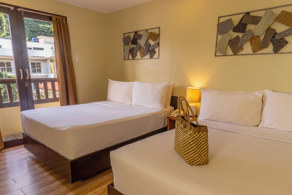 A hotel room with two beds, a balcony, and artwork on the walls.