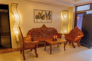 A wooden sofa with intricate carvings, a matching armchair, a small table, and decorative wall art. - Serene La Playa (Malay)