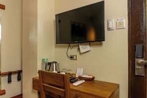 A hotel room with a wooden desk, a television mounted on the wall, a door with a lock, and a small sign on the wall. - Serene La Playa (Malay)