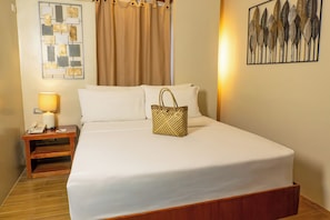 A neatly made bed with white linens, a wooden nightstand with a lamp, and a decorative wall piece. - Serene La Playa (Malay)