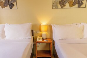 Ein Hotelzimmer mit zwei Betten, einer Nachttischlampe, einem Telefon und einem kleinen Tisch.