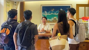 A group of people standing in a lobby with a wooden floor, a painting on the wall, and a reception desk. - Serene La Playa (Malay)