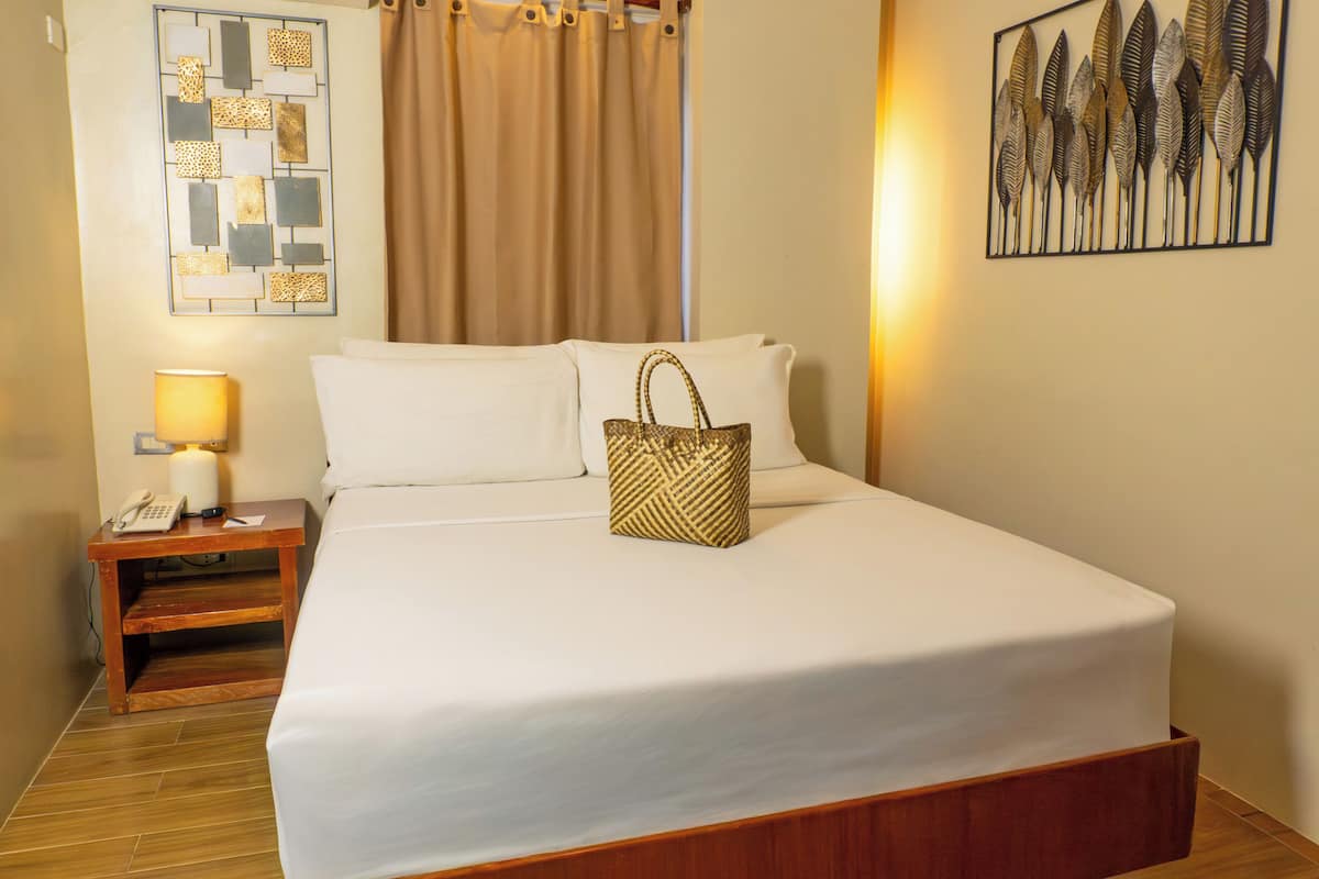 A neatly made bed with white linens, a wooden nightstand with a lamp, and a decorative wall piece.