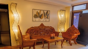 A wooden sofa with intricate carvings, a matching armchair, a small table, and decorative wall art. - Serene La Playa (Malay)