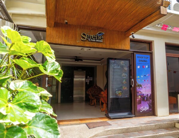 A restaurant entrance with a wooden canopy, a glass door, and a menu board advertising 'Rooftop Dining' hours. - Serene La Playa (Malay)