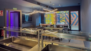 Restaurante moderno com divisória de vidro, mobiliário metálico e arte abstrata nas paredes.