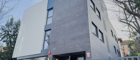 Un bâtiment moderne à la façade grise, doté de grandes fenêtres et d’un panneau d’alarme incendie bien visible.