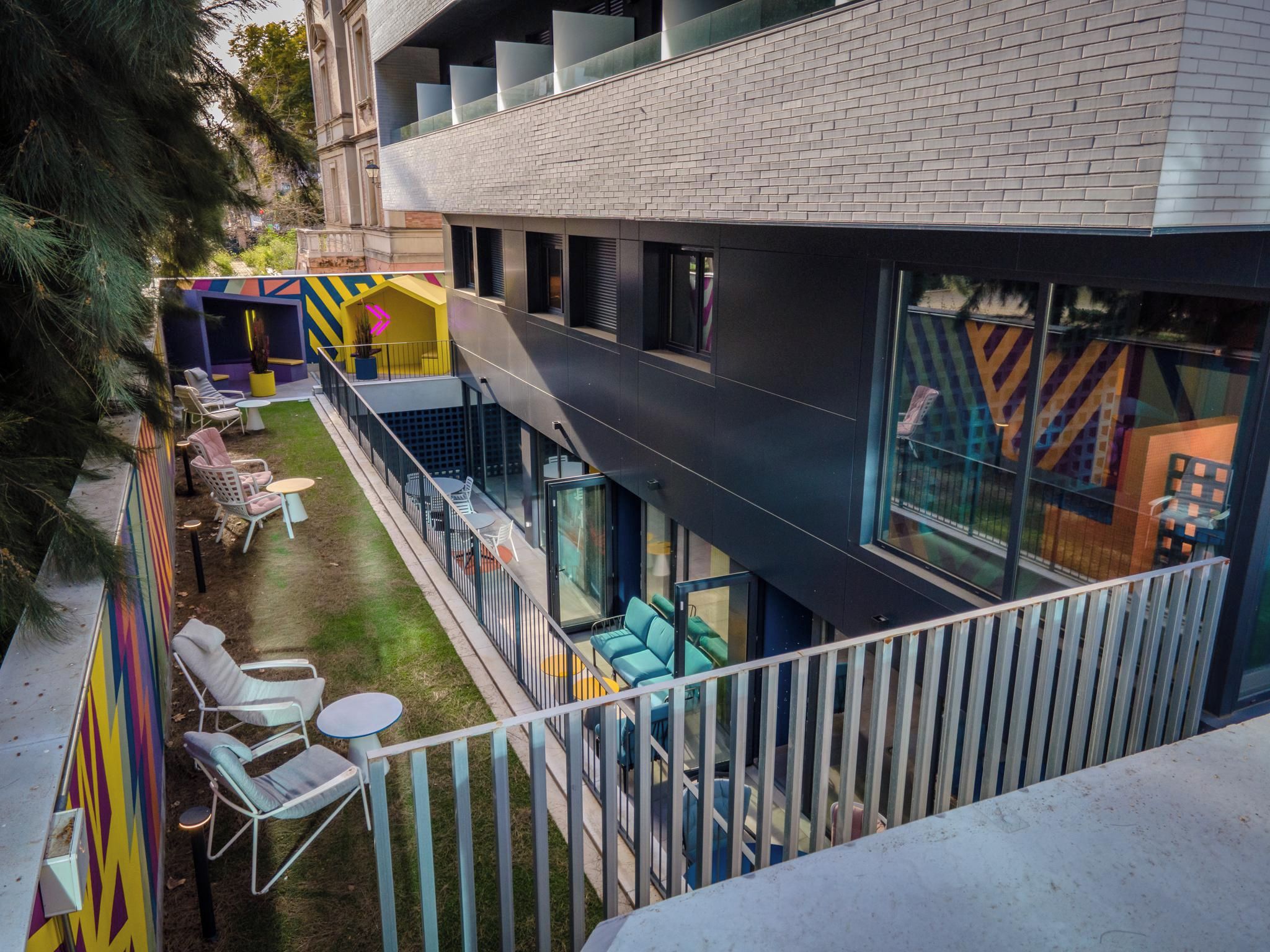 A modern building with a flat roof, large windows, and a balcony with outdoor seating.