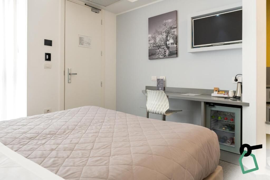 A hotel room with a bed, a desk with a chair, a television, and a mini-fridge.