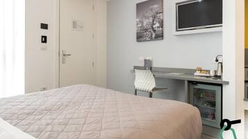 A hotel room with a bed, a desk with a chair, a television, and a mini-fridge.