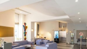 Un moderno vestíbulo de hotel con sofás, una televisión, una recepción y una escultura decorativa.