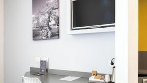 Una habitación moderna con escritorio, silla, televisor de pantalla plana y una obra de arte en la pared.