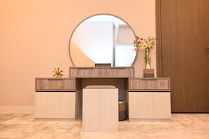 A room with a round mirror, a vanity with drawers, a bench, and a vase with flowers. - Riyadh Inn Hotel (Riyadh)