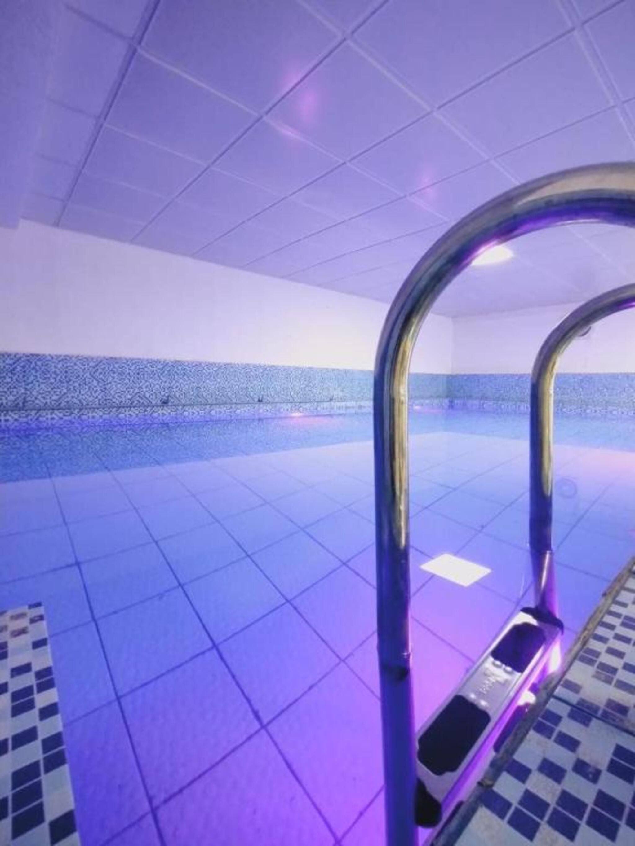 Una piscina con suelo de baldosas y una escalera metálica.