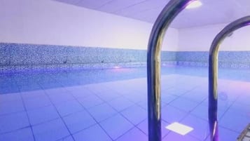 Una piscina con suelo de baldosas y una escalera metálica.