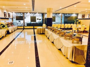 Un gran saló de banquetes amb taules preparades per a un esdeveniment formal, una paret decorativa i un sòl polit.