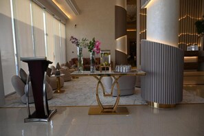 A modern lobby with a marble floor, a gold and black pedestal, a round table with vases, and a large cylindrical column. - Riyadh Inn Hotel (Riyadh)