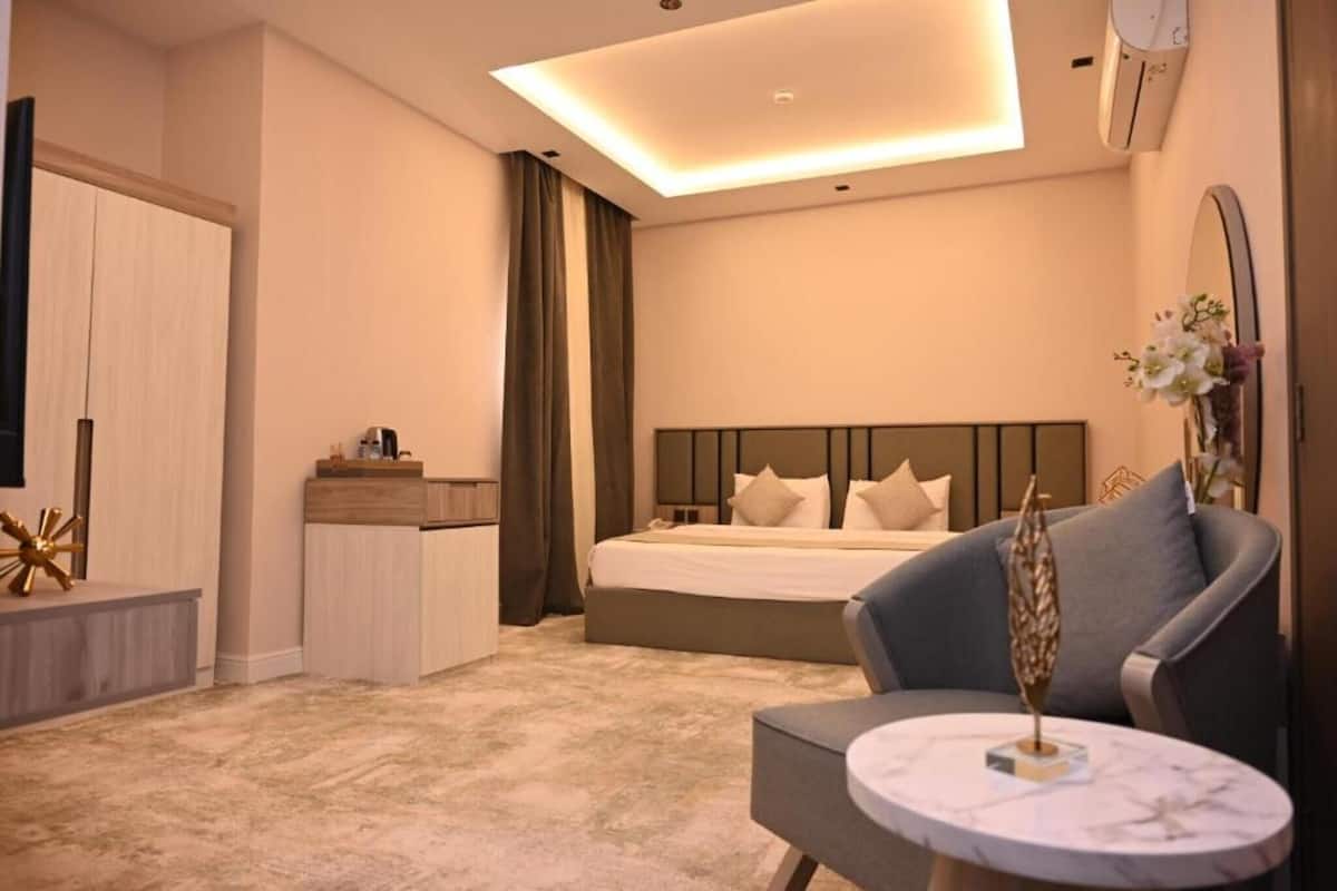 Una habitación de hotel moderna con una cama, un área de descanso con una mesa, un armario y un espejo.