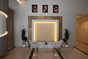 A lobby with a reception desk, two white armchairs, a small round table, and three framed portraits on the wall.