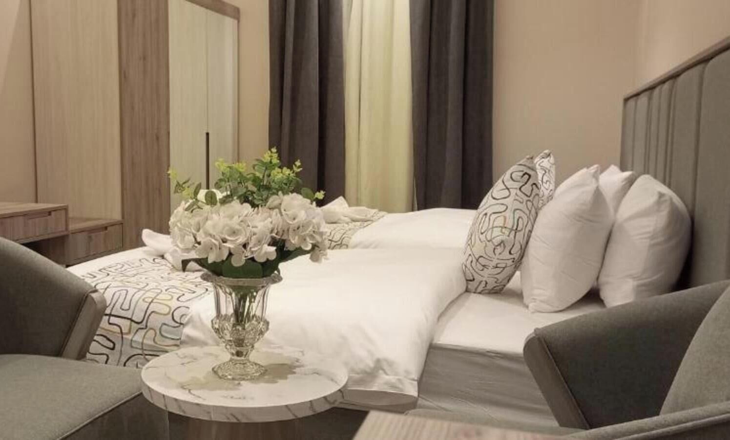 Quarto de hotel com uma cama, uma mesa redonda com um vaso de flores e duas poltronas.