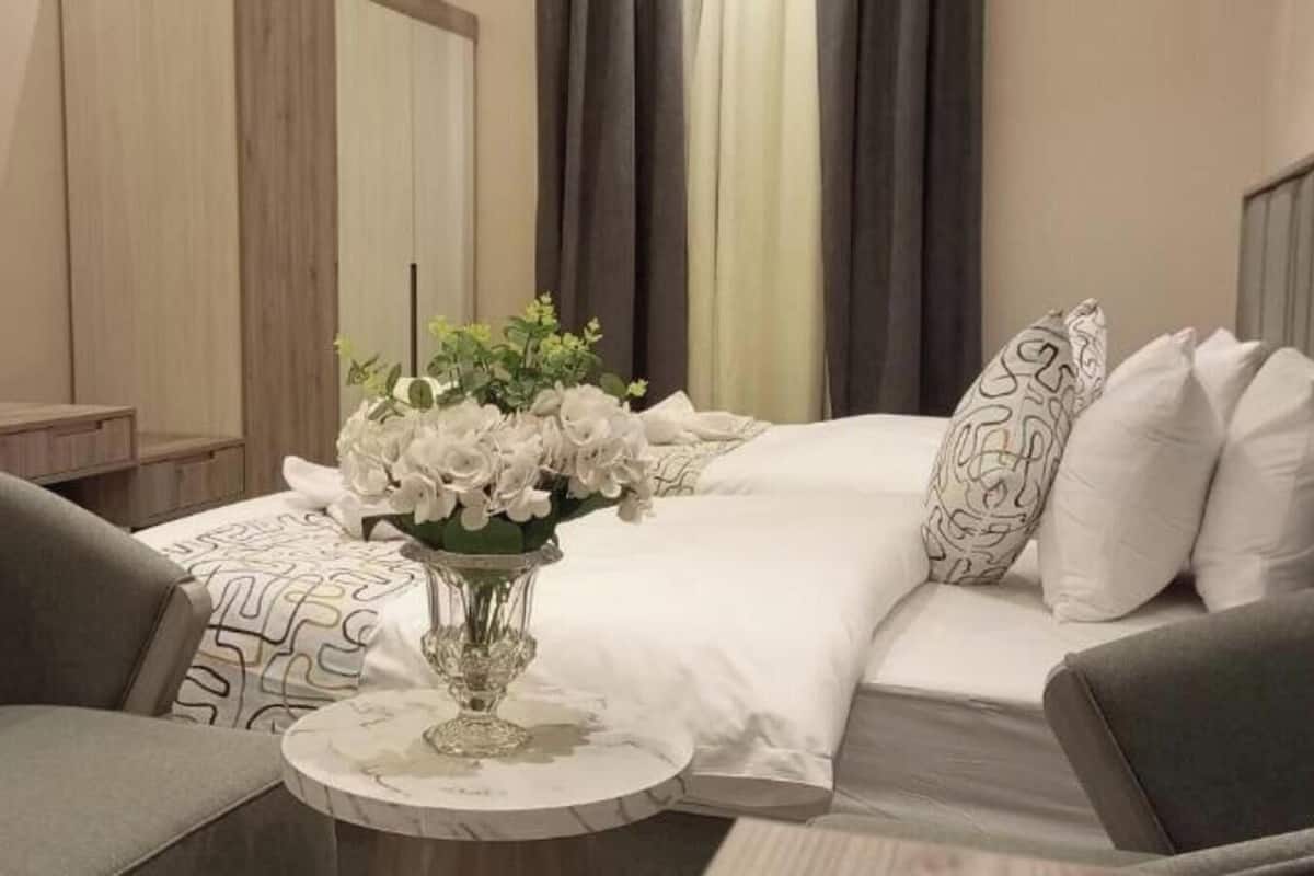 Una habitación de hotel con una cama, una mesa redonda con un florero y dos sillones.