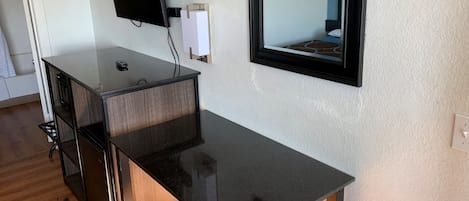 Une pièce avec un bureau noir, un téléviseur à écran plat fixé au mur, une petite table et une chaise.