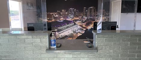 Zona de recepción con un mural de paisaje urbano, dispensador de gel antibacterial y una computadora Lenovo.