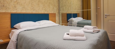 A neatly made bed with a quilted blanket, a wooden headboard, and a mirror reflecting the room.