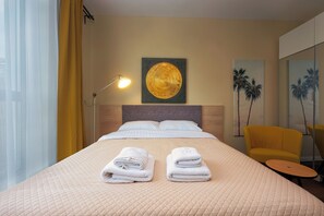 Une chambre d’hôtel avec un lit, deux serviettes, une lampe, un tableau, une chaise et un miroir.