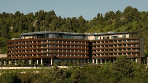 A modern multi-story hotel with a flat roof, surrounded by dense forest. - Beldersoy Resort And Spa (Tashkent)