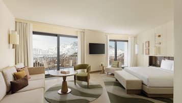 A hotel room with a bed, sofa, armchair, a small table, and a TV.