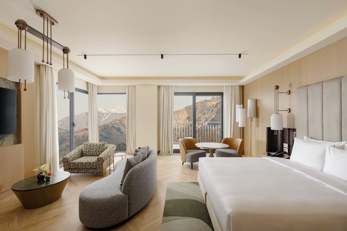 A hotel room with a large bed, a sofa, a chair, a small table, and a TV.