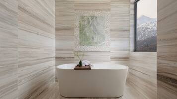 A modern bathroom with a freestanding bathtub, a decorative wall piece, and a view of a snowy mountain through a window.