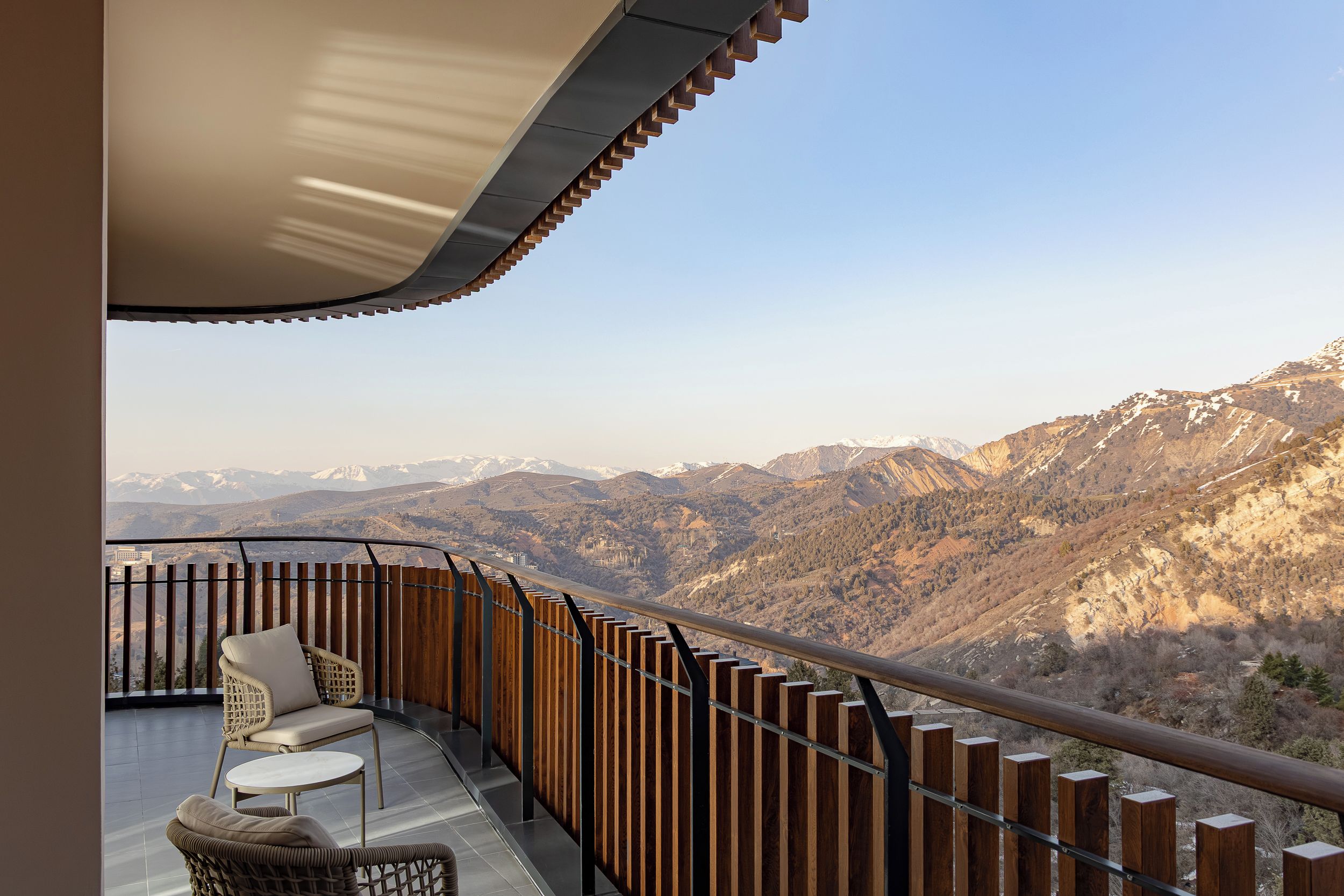 A balcony with a view of mountains, a chair, and a table.