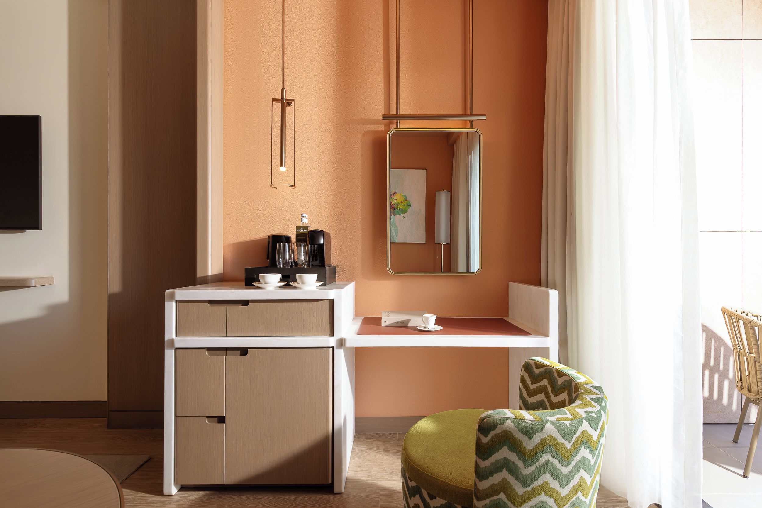 A hotel room with a desk, a chair, a mirror, and a television.