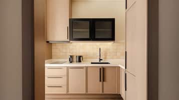 A modern kitchen with light wood cabinetry, a black range hood, and a tiled backsplash.