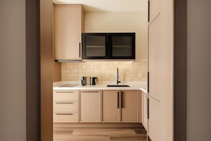 A modern kitchen with light wood cabinetry, a black range hood, and a tiled backsplash.