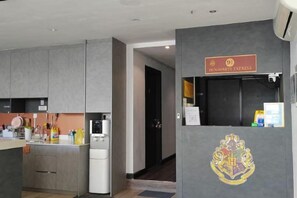A modern kitchen with grey cabinets, a refrigerator, and a coffee machine. There is a sign with a crest on the wall. - C YOU Rooms (Semporna)