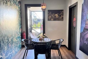 A dining area with a table and chairs, a hanging light fixture, and a door leading to an outdoor space. - C YOU Rooms (Semporna)