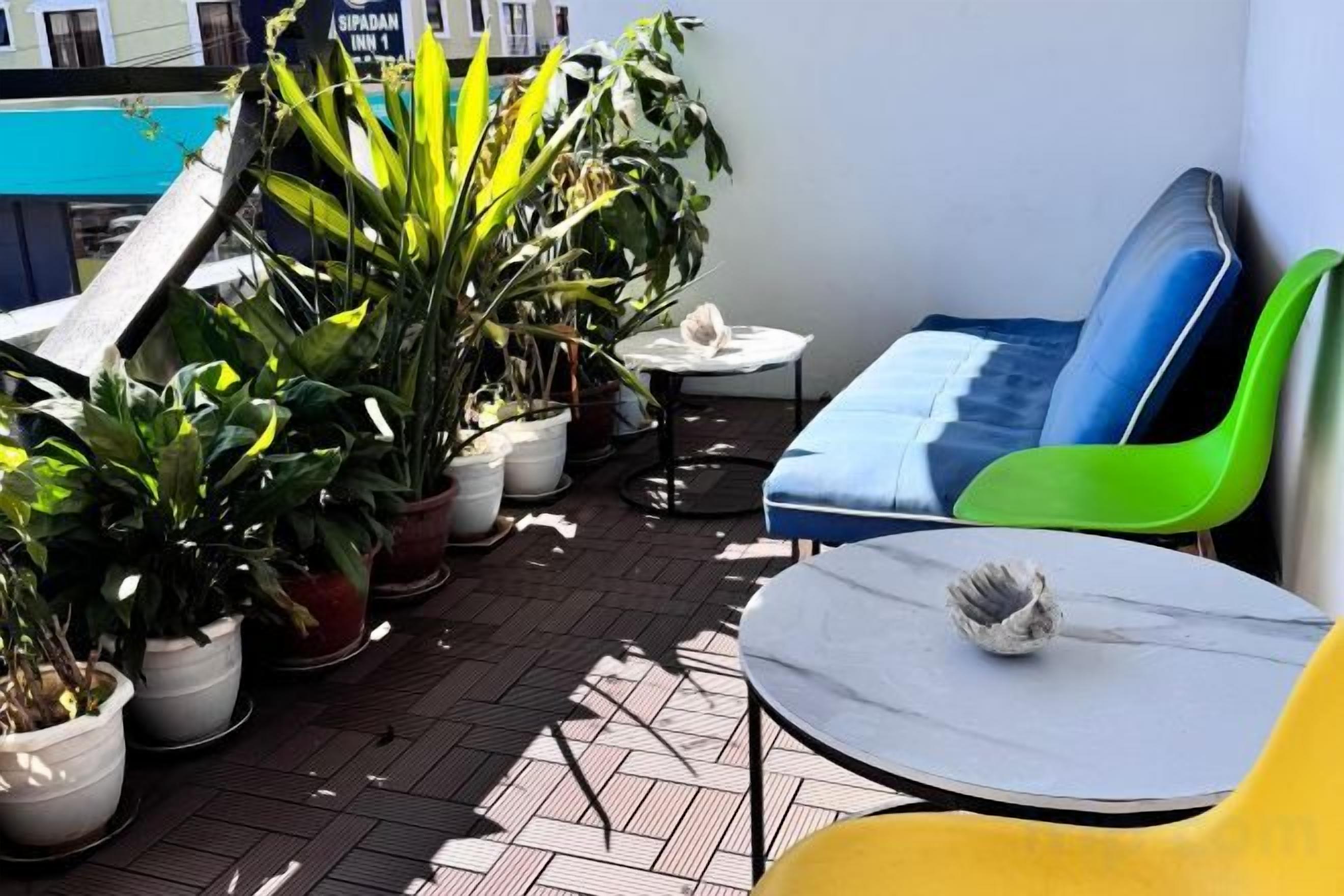 A rooftop terrace with potted plants, a table, and colorful chairs.