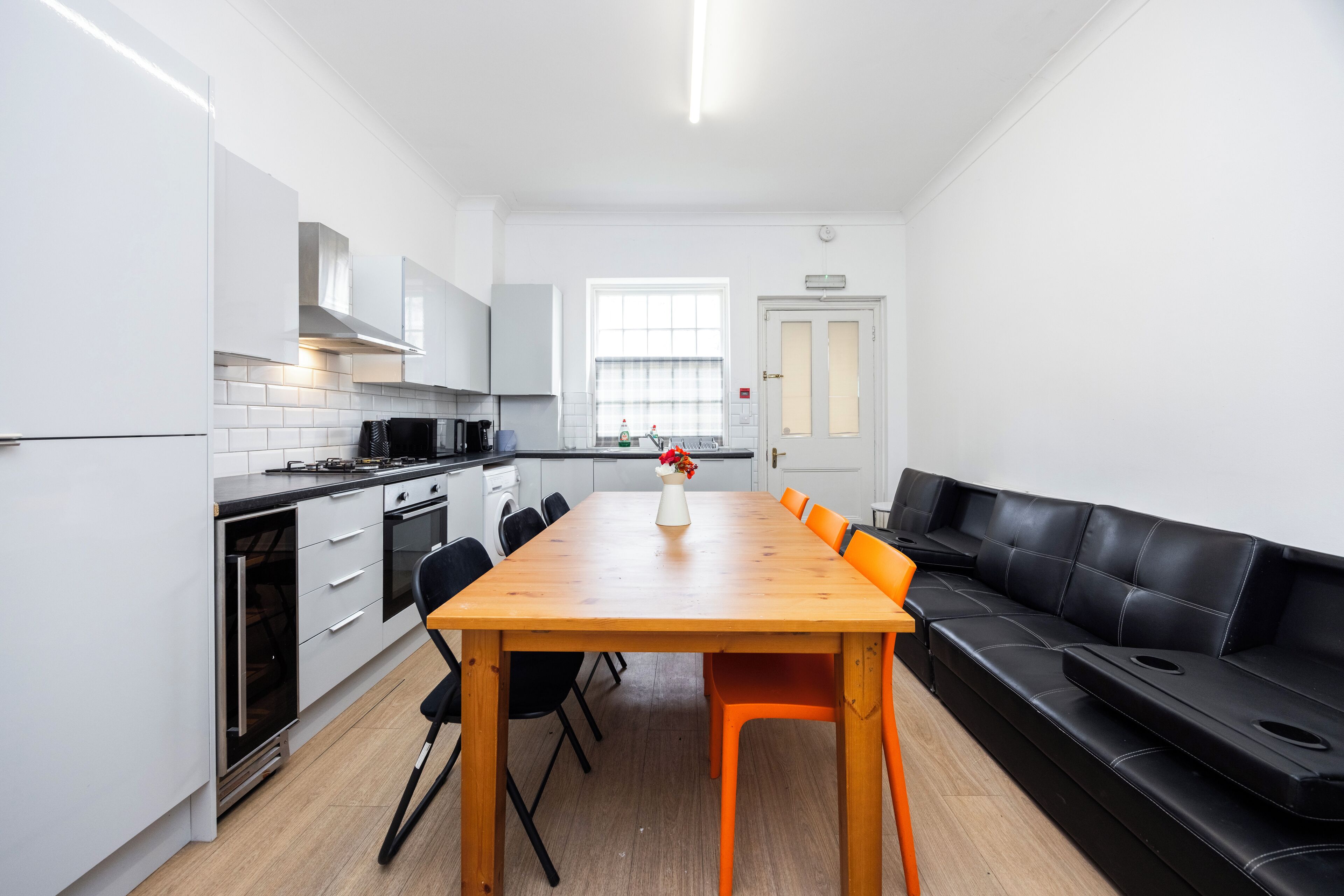 A modern kitchen with white cabinets, a wooden table, and a black leather couch.