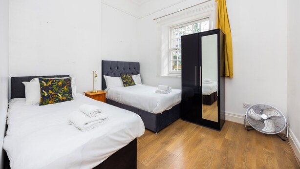 Una habitación de hotel con dos camas, un espejo, un ventilador y una ventana con cortina amarilla.