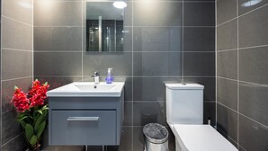 Un baño moderno con un lavamanos, espejo y retrete blancos, además de un cubo de basura.