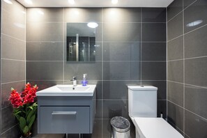Ein modernes Badezimmer mit einem weißen Waschbecken, Spiegel und einer Toilette sowie einem Mülleimer.