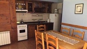A kitchen with wooden cabinets, a stove, a refrigerator, and a dining table with chairs.