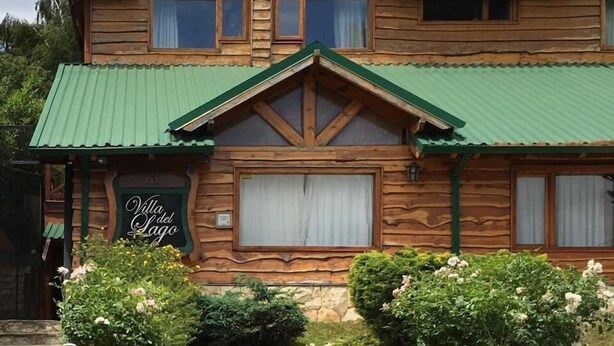 A wooden villa with a green roof, multiple windows, and a sign reading 'Villa del Lago'.