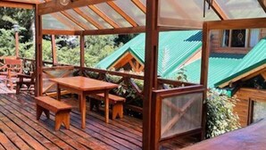 A wooden deck with tables and benches, a glass ceiling, and a view of green-roofed buildings.